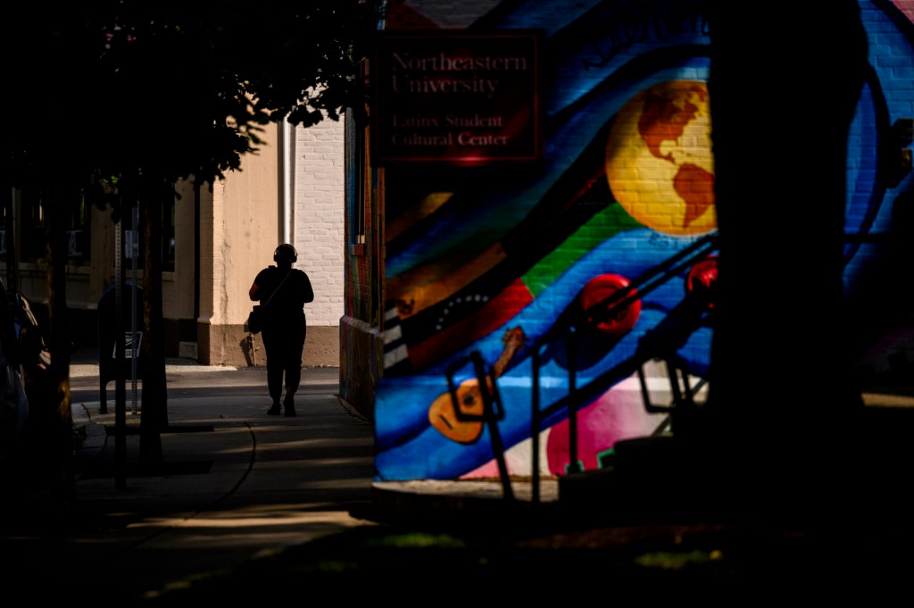 A person walks in the shade on a sidewalk outside on a sunny day.