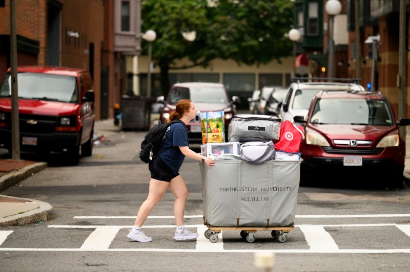 A student pushes a full rolling big across a crosswalk