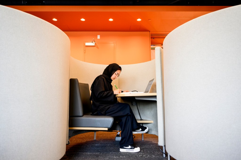 A person studies in a white cubicle with an orange light overhead.