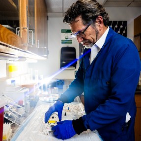 Craig Ferris working in a lab wearing a blue lab coat, safety goggles, and blue gloves.