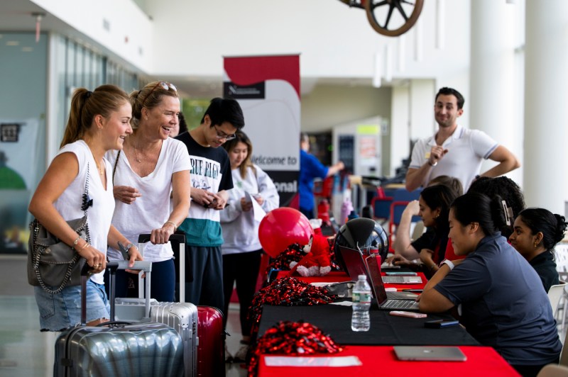 People line up with baggage at a help desk in International Village