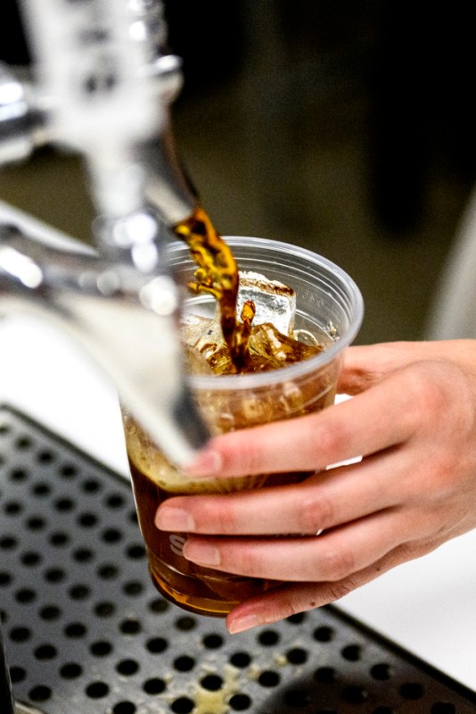 A student pouring cold brew into a plastic cup. 