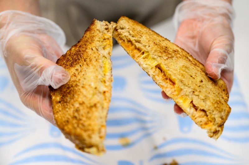 A student wearing gloved hands holding a grilled cheese. 