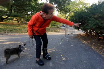 A woman wearing a red jacket walking a dog on a leash points to where she discovered a dead bear in Central Park.