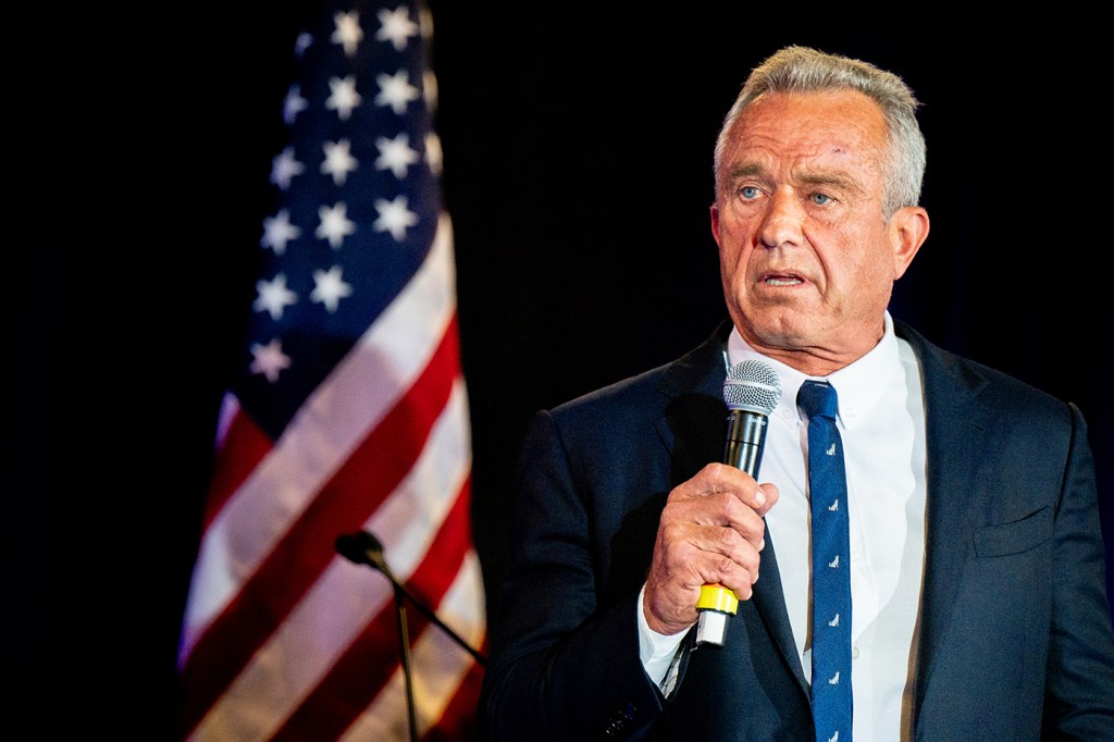 RFK Jr speaking into a microphone in front of the United States flag.