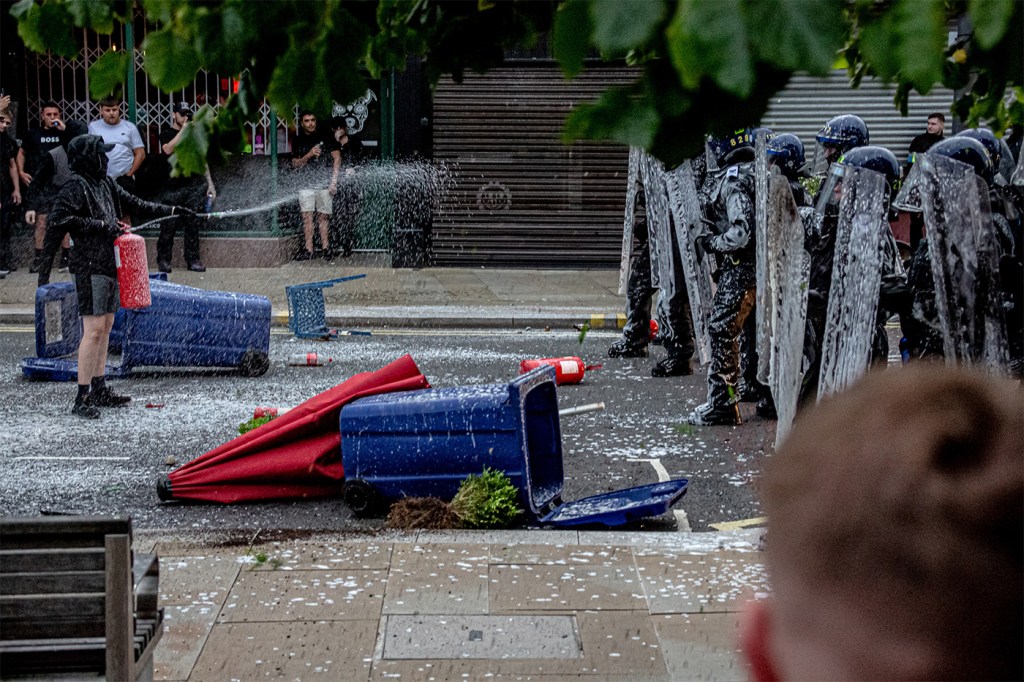 On a looted street, a person sprays a fire hydrant at uniformed officers.