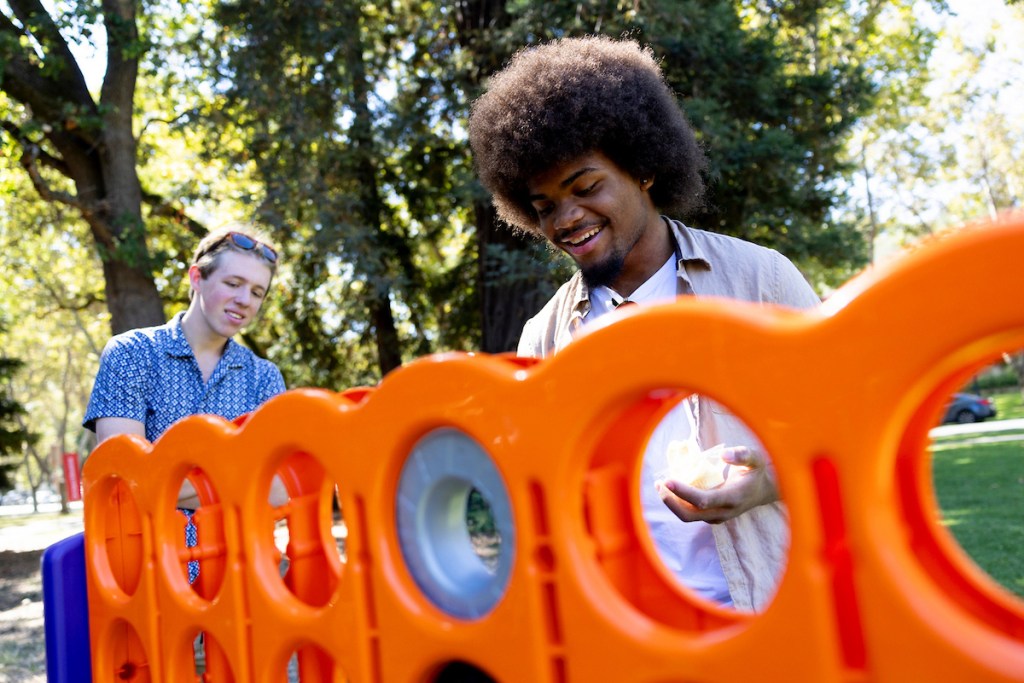 Two people play the game Connect 4 outside on a sunny day.