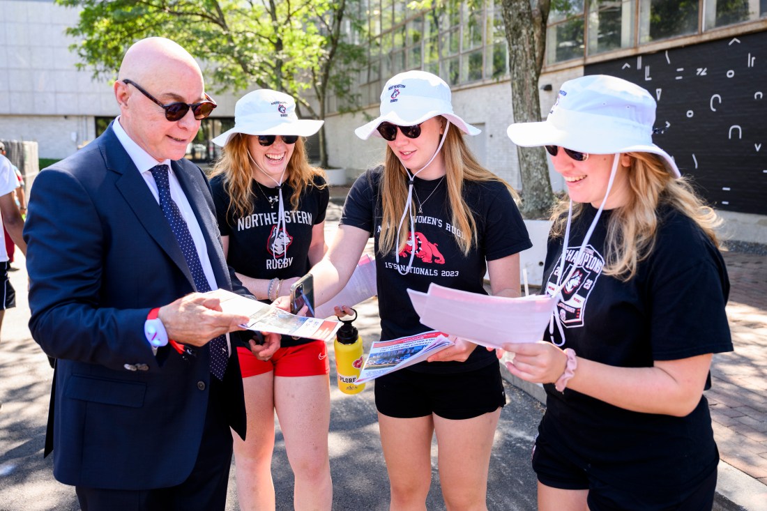 Three students wearing bucket hats pointing to a piece of paper that President Aoun is holding in one hand.