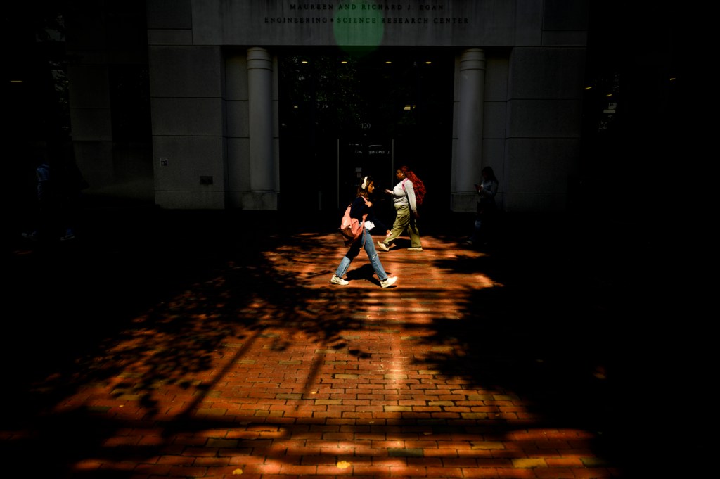 Two people walk into the bright sunlight and back toward the shadows.