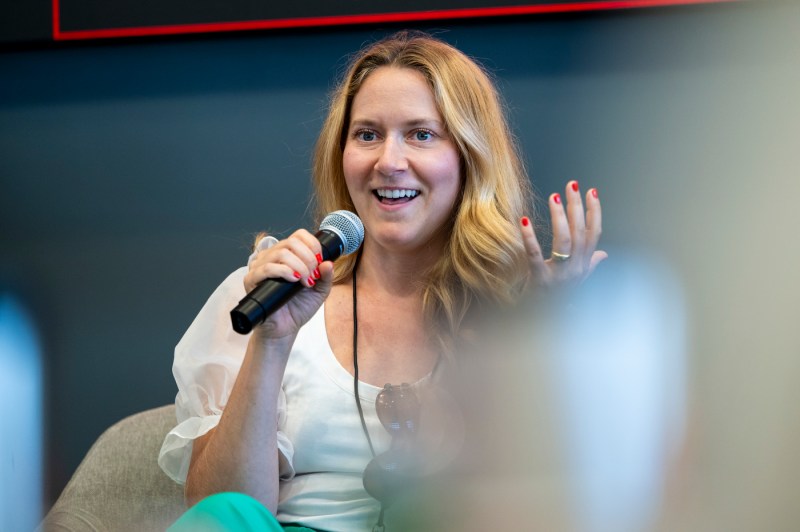 Emily Schario speaking into a microphone and gesturing with one hand. 