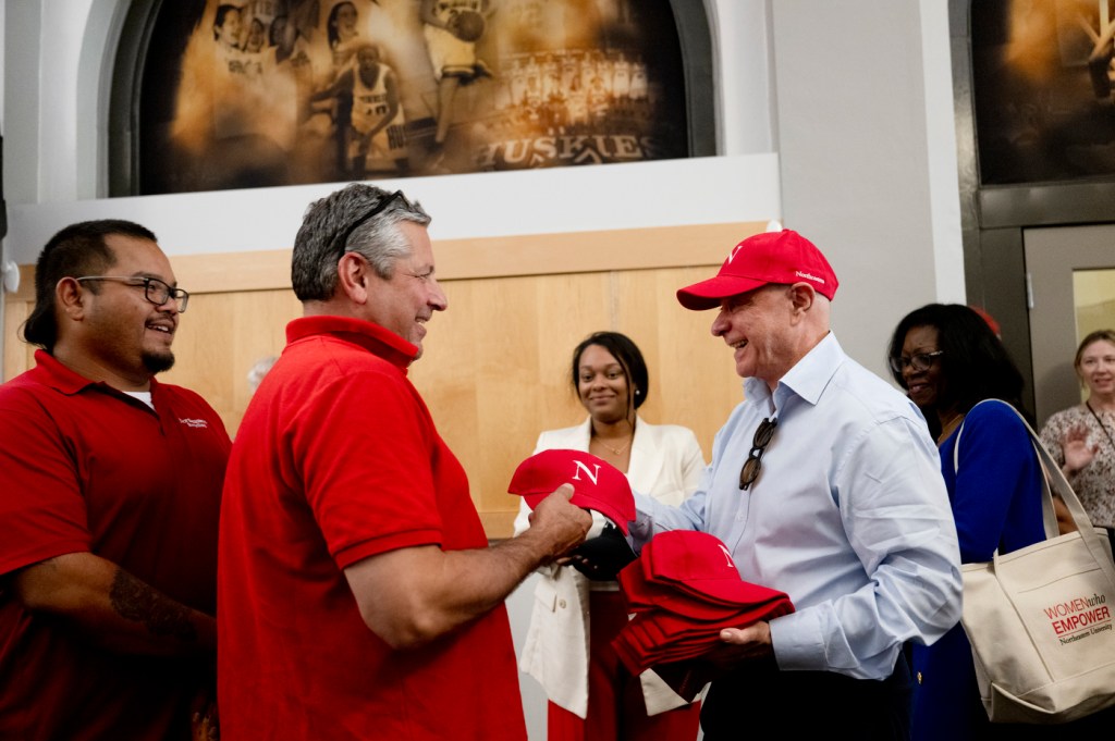 President Aoun handing a red baseball cap to a facilities worker wearing a red polo shirt.