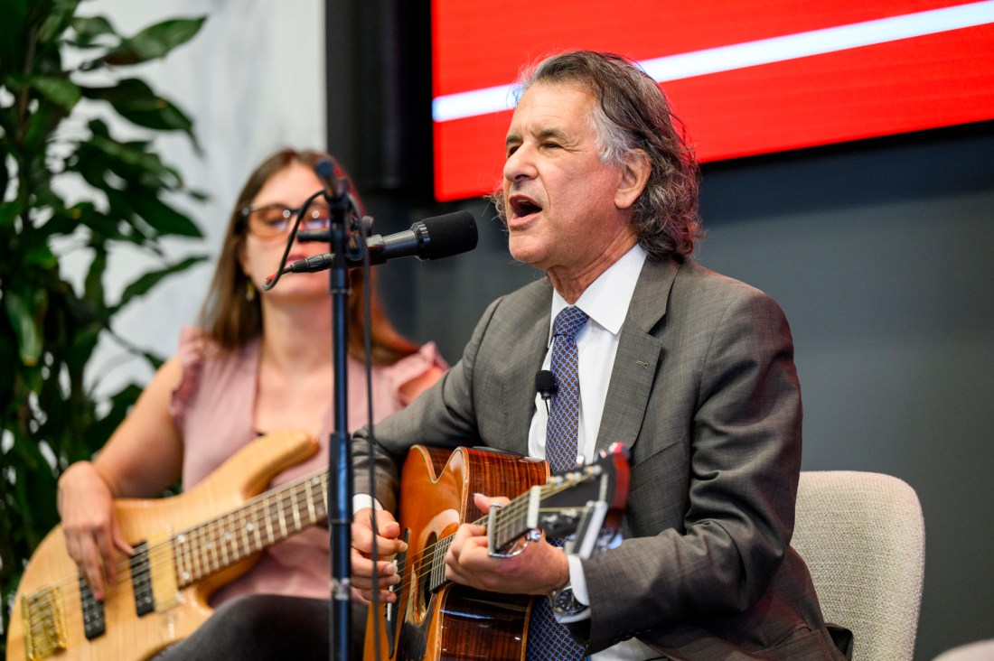 Daniel Levitin playing a guitar and singing on stage at the Presidential speaker series.