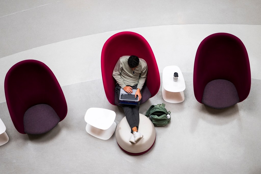 A student sitting in a red chair in ISEC working on their laptop.