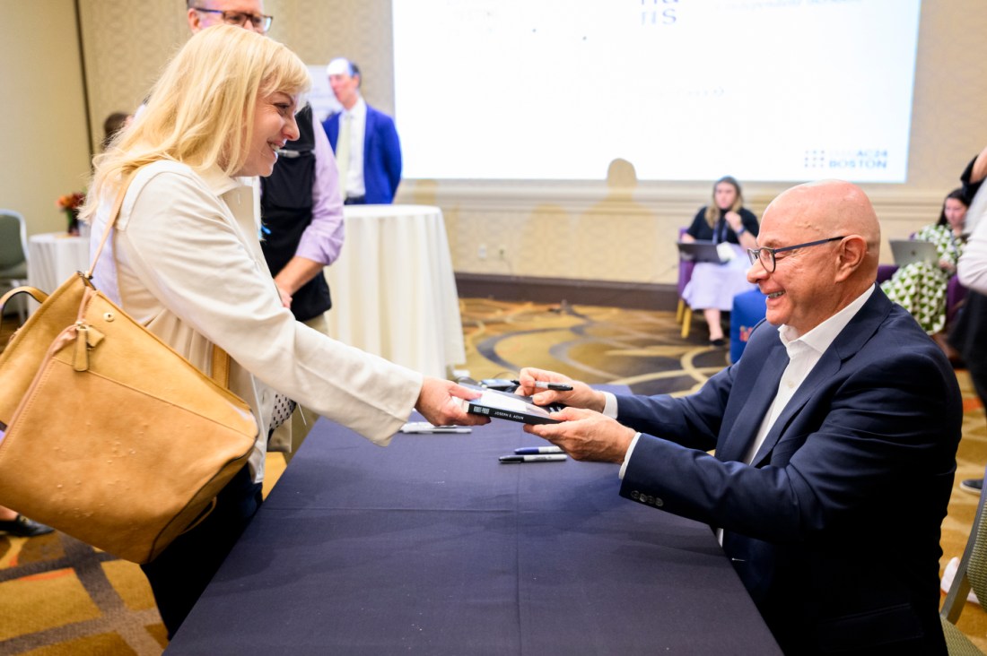 President Aoun receiving a copy of his book 'Robot Proof' to sign from a person with blonde hair smiling at him.