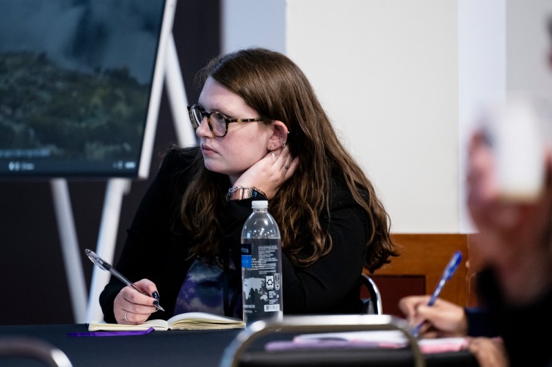 A student resting their hand on their neck while taking notes at a Symposium.