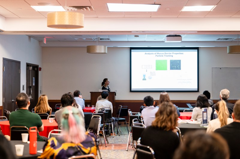 Rebecca Carrier speaking at the front of a classroom at a Symposium.