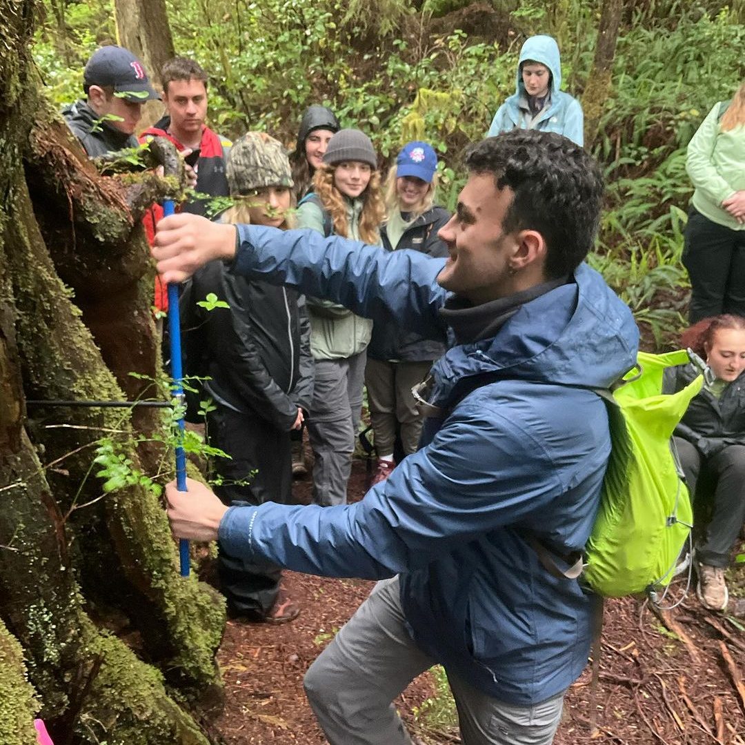 A student holding a blue stick-like tool up to a tree.