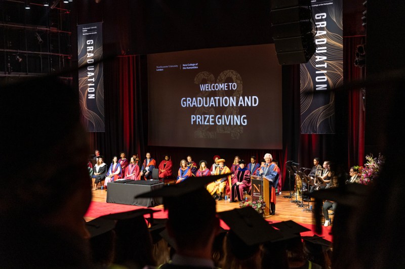 Faculty members and Principal AC Grayling on stage at the London graduation in front of a screen that says 'Welcome to Graduation and Prize Giving'.