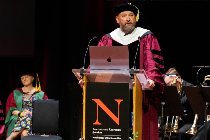 A faculty member speaking into the microphone at a podium at the London graduation.