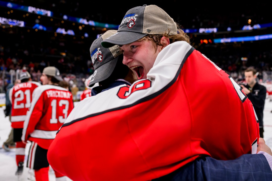 Cameron Whitehead hugging someone out of excitement while inside a hockey arena.