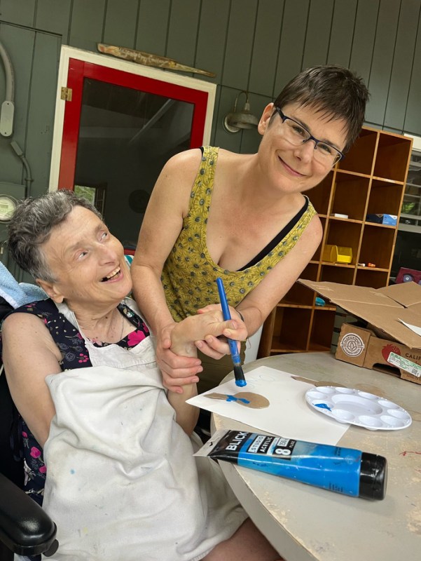 Kim Ho holding the hand of a person with disabilities as they paint on a sheet of paper.