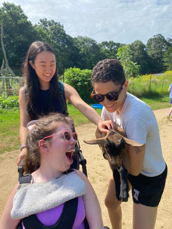 Students holding a goat up to a person with disabilities. 