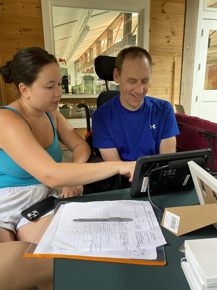 A student sitting next to a person with disabilities, pointing to the screen of an iPad.