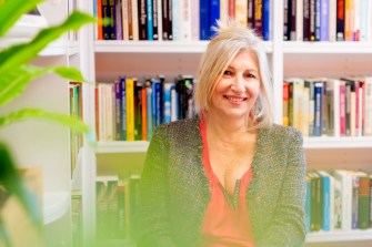 Portrait of Deborah Walker in front of a colorful bookshelf.