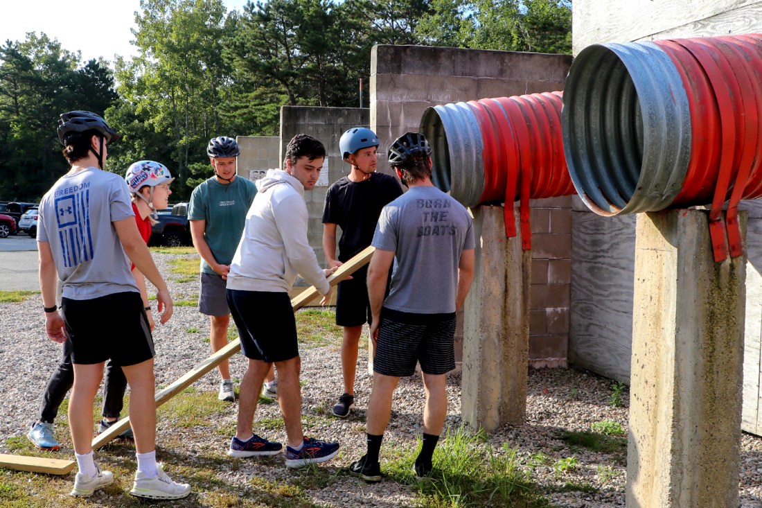 Six people standing in front of a large pipe several feet off the ground.