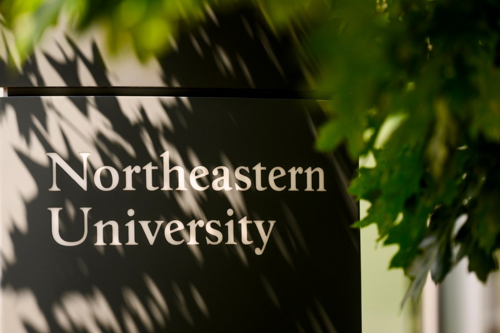 Northeastern University logo on a building next to a tree.