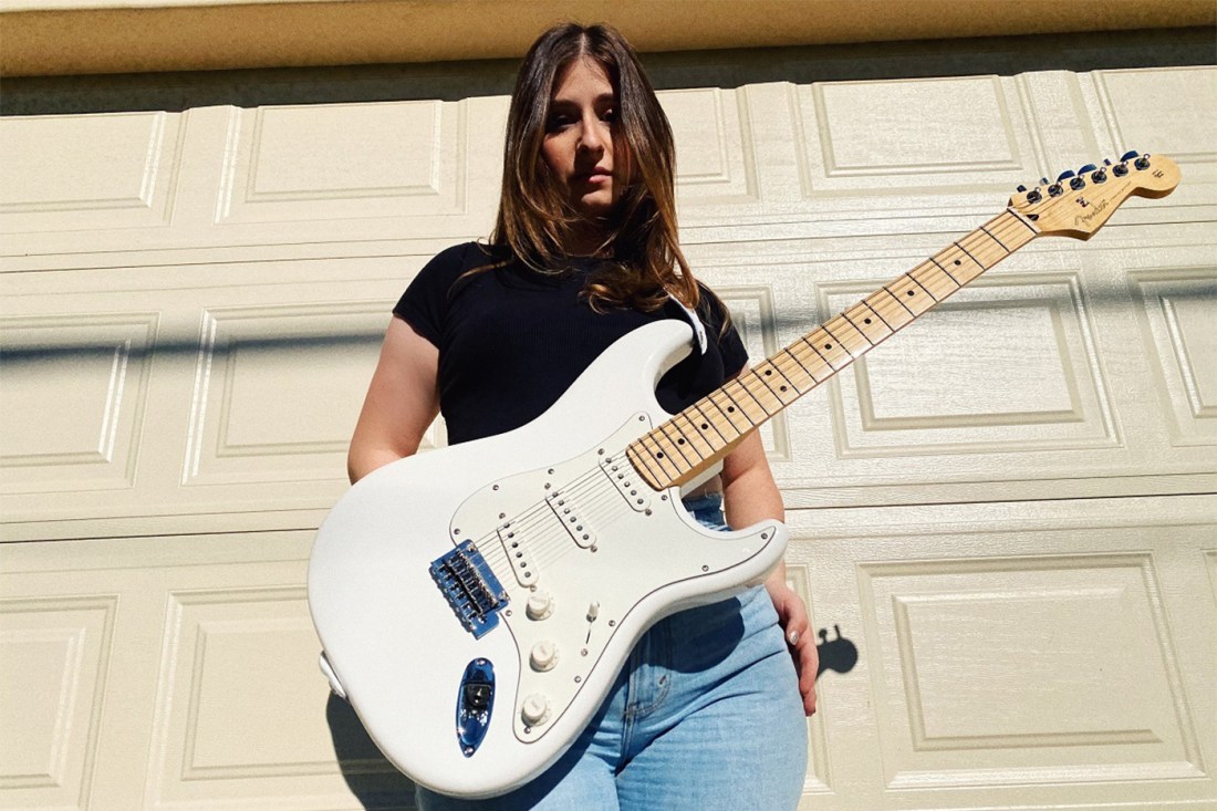 Annie Schindel posing in front of a garage door with a white electric guitar.