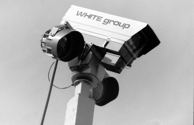 A black and white photo of a security camera with a 'White group' label on it.