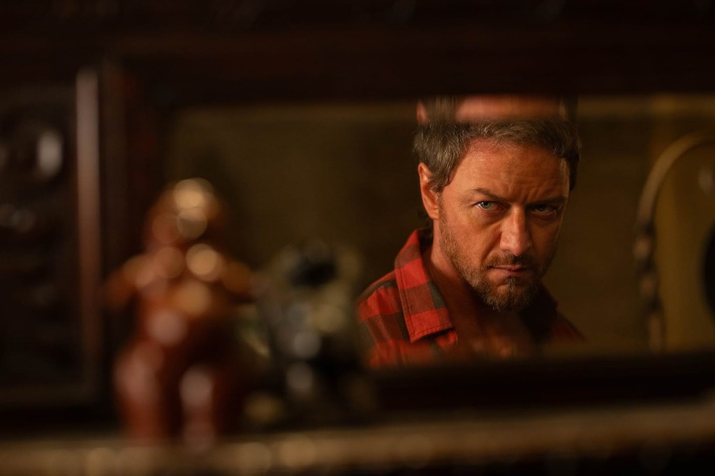 A screen capture from the movie 'Speak No Evil' that shows James McAvoy staring into a mirror wearing a red flannel shirt.