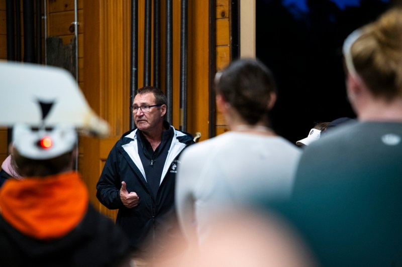 A coach motivates student-athletes in the boathouse, inspiring the rowing team.