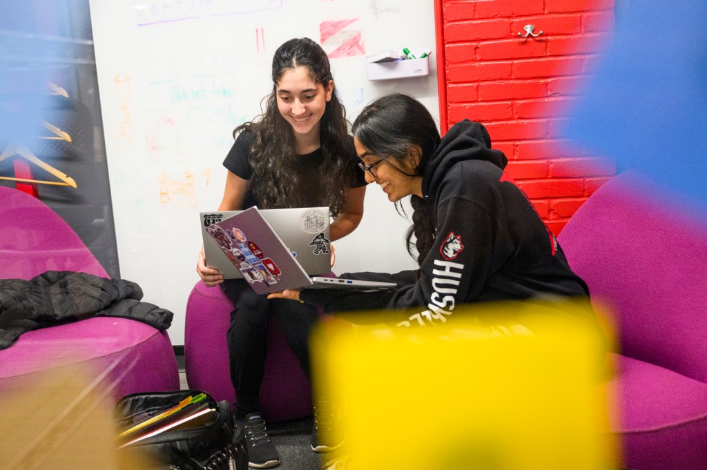 Two students collaborating together with their laptops in their laps.