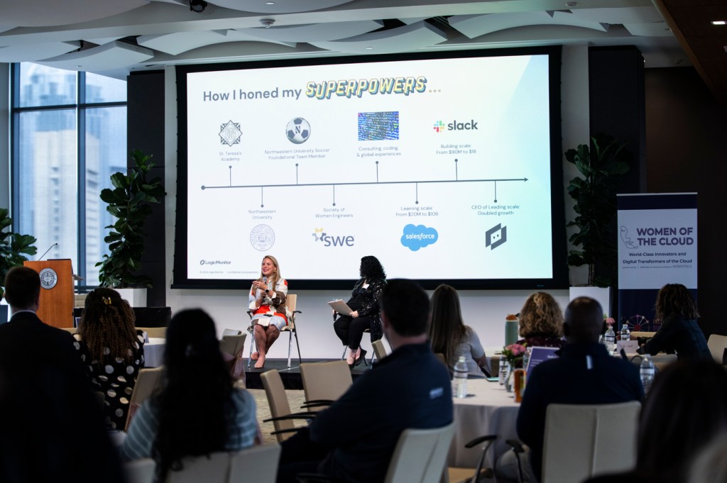 A panel of speakers sitting in front of a an audience members discussing a slide with a timeline on it.