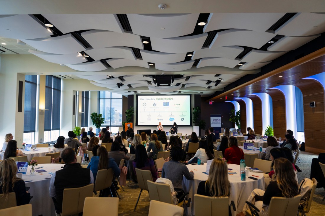 A room full of people listening to two speakers at the front of the room.