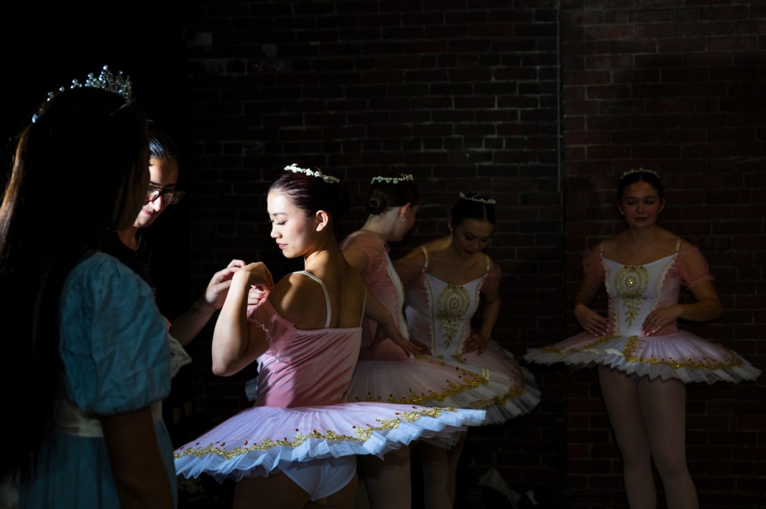 A ballet company rehearsing dance routines inside a studio with dancers in classical ballet attire.