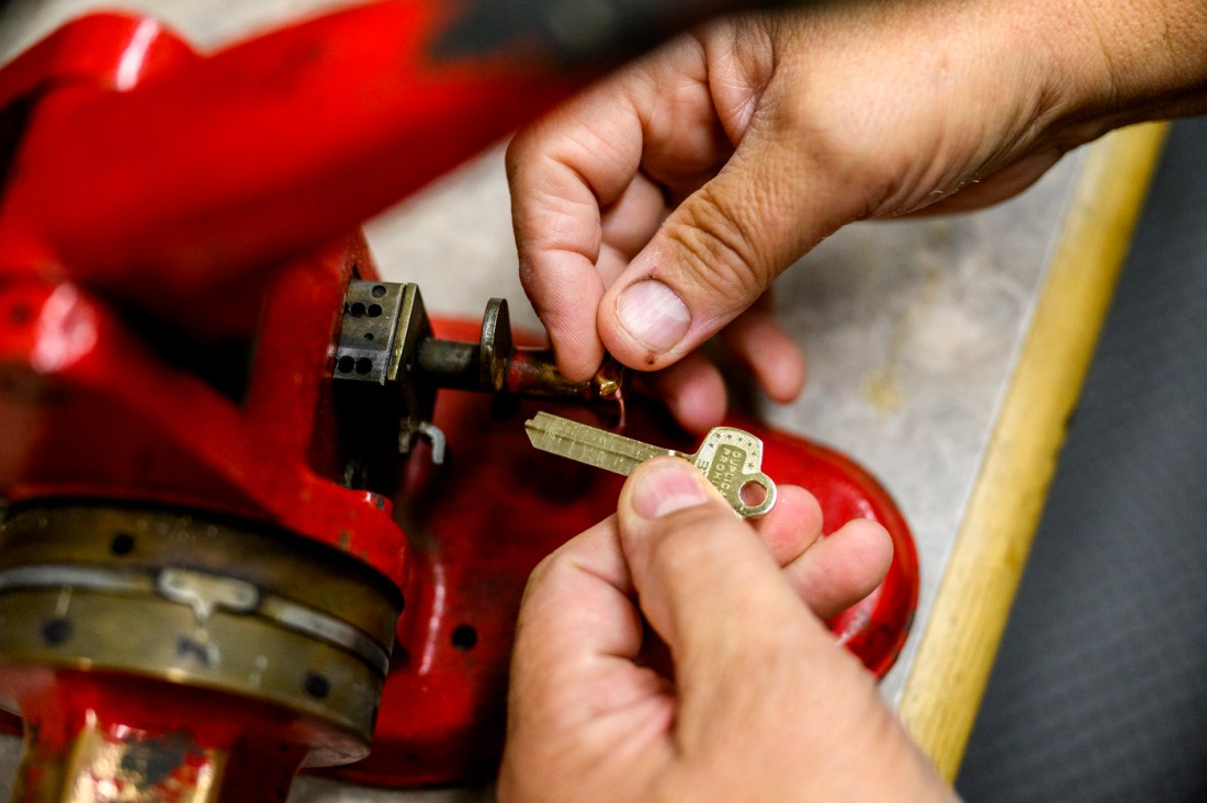 Hands of a locksmith working on a small piece of equipment with tools nearby.
