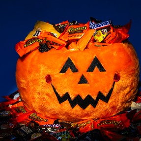 A stuffed Halloween pumpkin covered with and surrounded by candy.