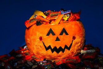 A stuffed Halloween pumpkin covered with and surrounded by candy.