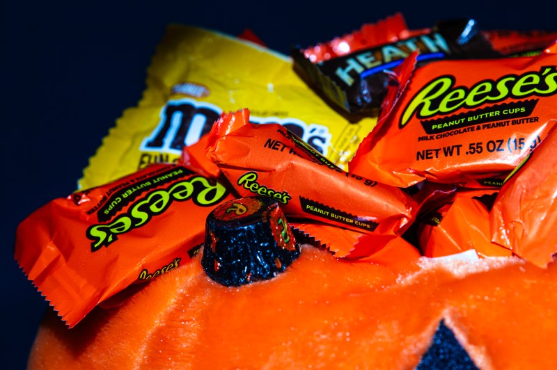 A stuffed orange pumpkin with a pile of Reese's Peanut Butter Cups on top.