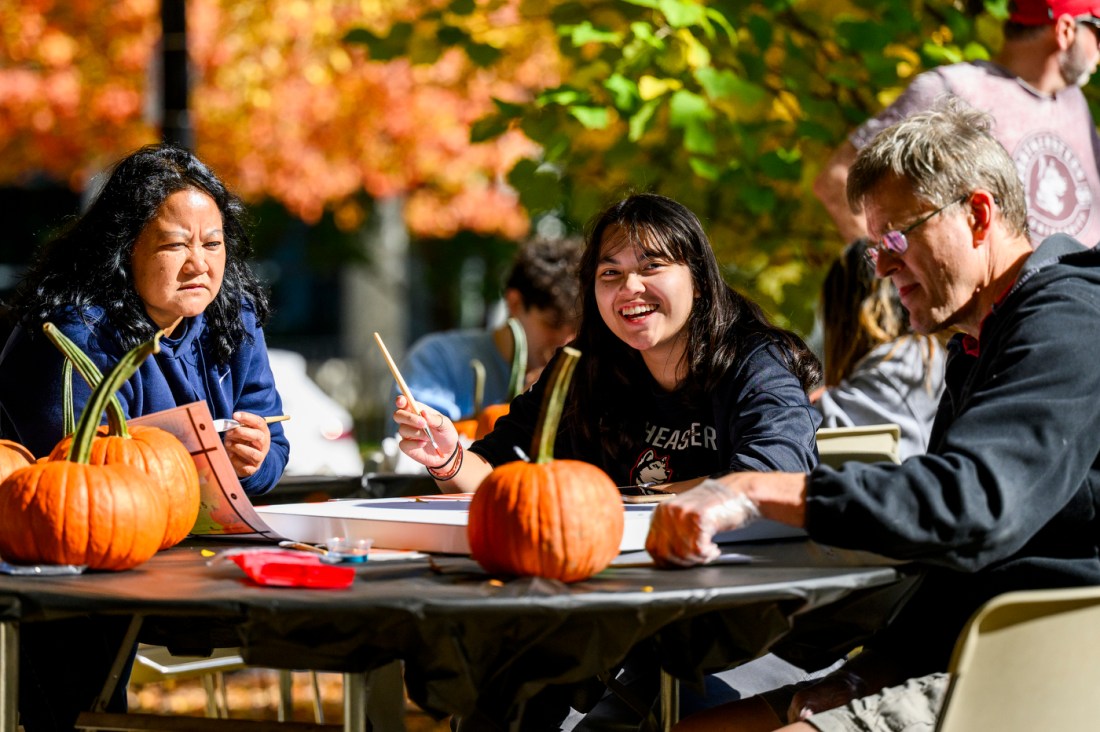 A student and their family sit at a table painting, surrounded by pumpkins. 