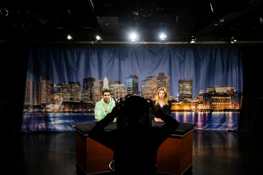 Armaan Sarah and Rachel Soloman sit as news anchors in the TV studio.