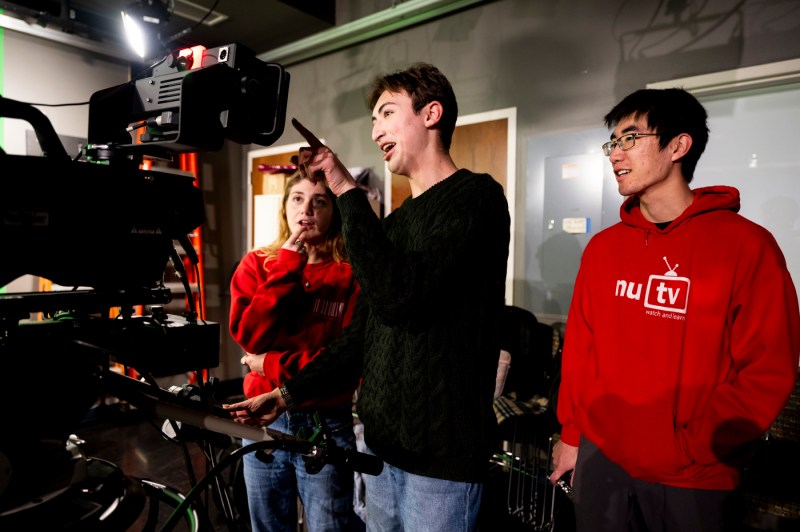 Caitlin Pronos, Andrew Longo, and Adam Viazanko looking at a camera during an NUTV recording. 