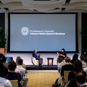 Speakers sitting on stage in front of an audience for a fireside chat.