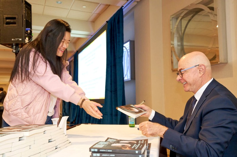 President Joseph Aoun signing a copy of his book for a person smiling at him.