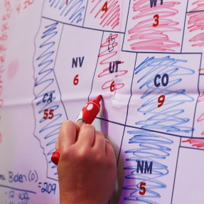 A hand holding a red sharpie coloring in a map of states in blue and red.