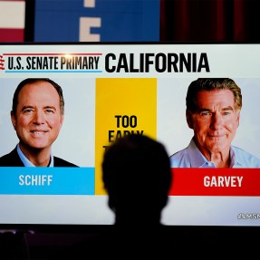 The silhouette of a person watching a TV displaying faces from a race in California.