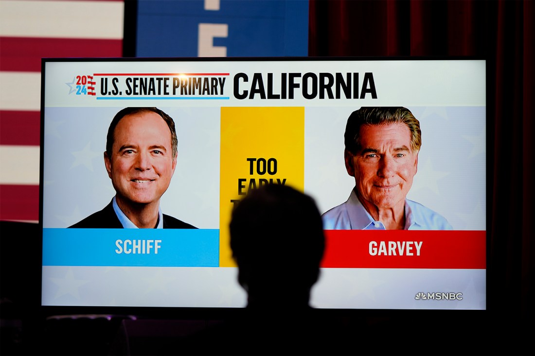 The silhouette of a person watching a TV displaying faces from a race in California.